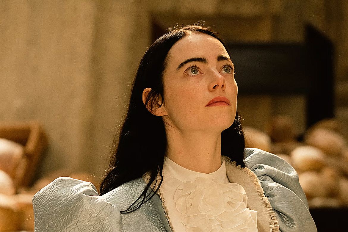 Emma Stone em cena de Pobres Criaturas (2023), vestindo um traje azul com detalhes brancos e olhando para cima em um ambiente clássico.